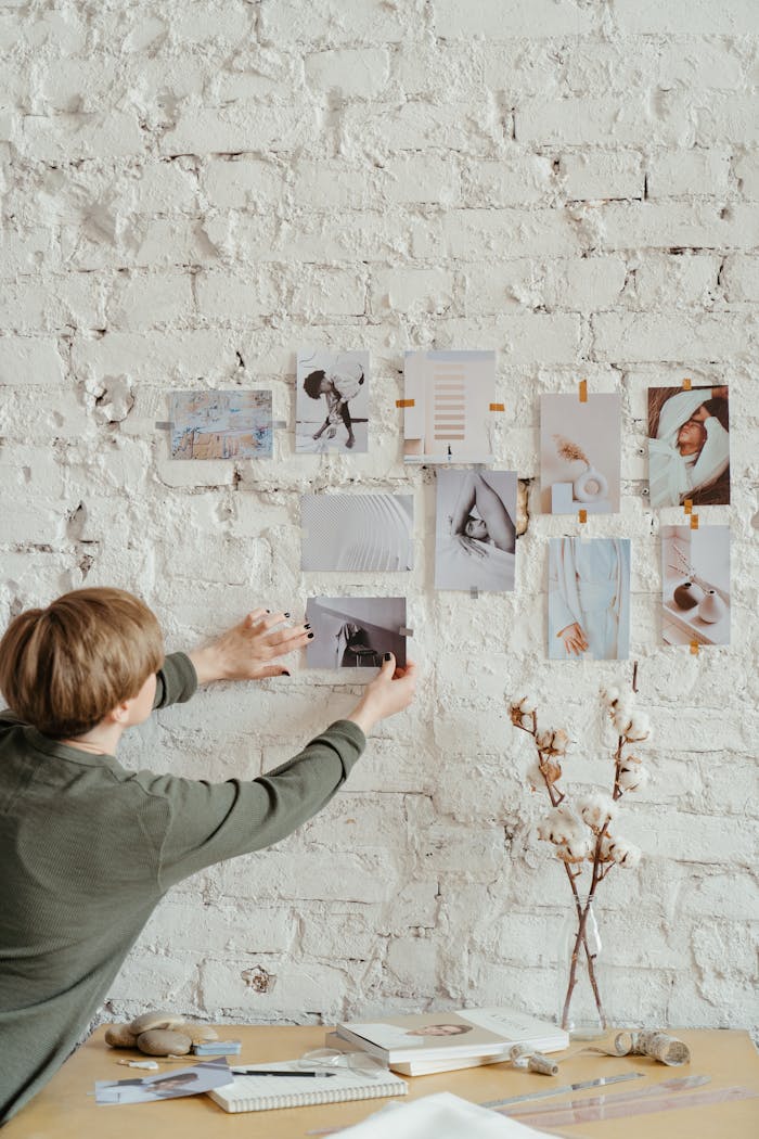 Person creating a mood board with photos on a white brick wall in a modern office setting.